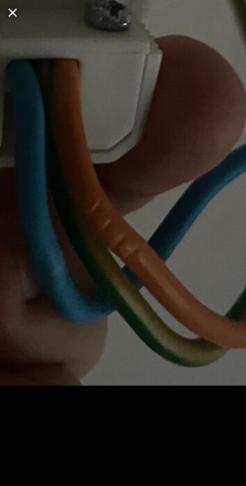 Närbild av färgade elsnören, blått, grönt och orange, anslutna till en vit plastkontakt med en metallskruv.