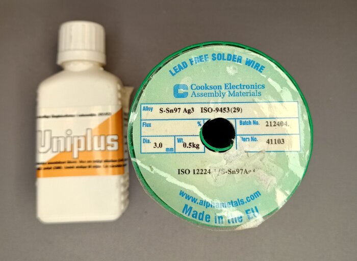 Rulle med blyfri lödtråd, S-Sn97 Ag3, och flaska med Uniplus-flussmedel på ett bord.