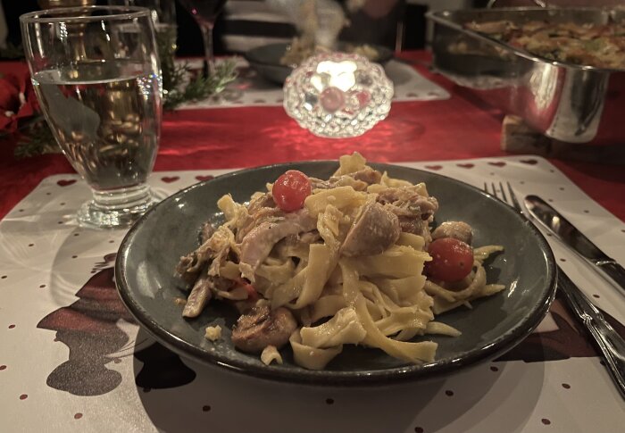 Pastagratäng med kyckling, ädelost, champinjoner, broccoli och tomat på en tallrik framför ett dukat middagsbord.