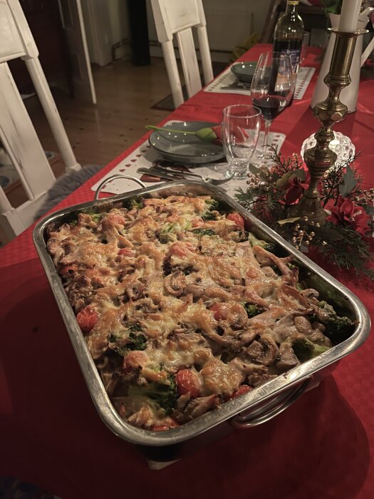 Pastagratäng med kyckling, ädelost, champinjoner, broccoli och tomat på ett dukat bord med röd duk och upplagt porslin.