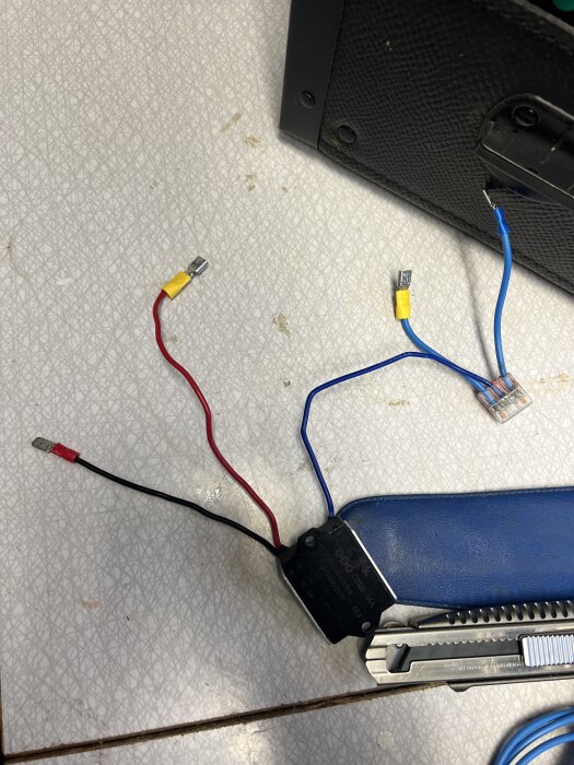 Elektriska kablar med anslutningar, en blå kapsling, en skruvmejsel och en svart plastlåda på ett bord.