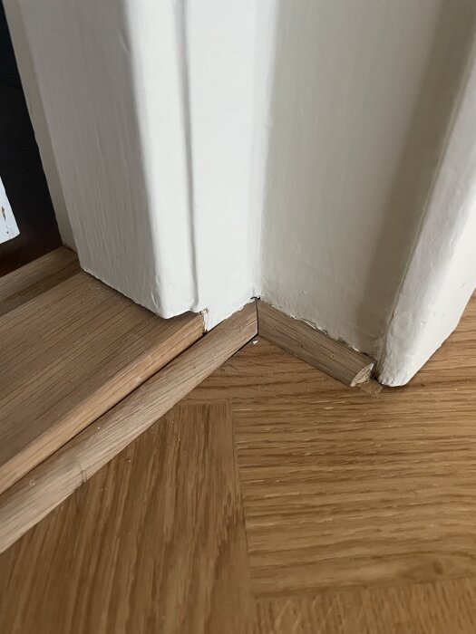 Parkettgolv installerat vid dörrkarm med en synlig glipa där golv och karm möts, samt en kvartsstav vid sockeln för finish.