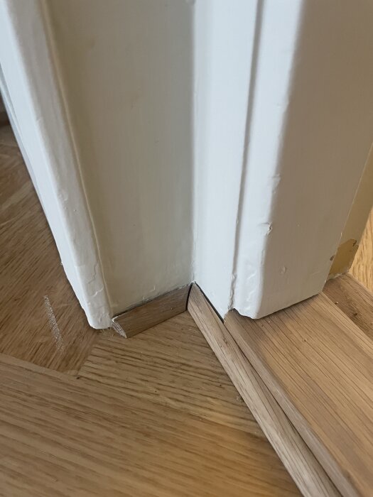Närbild av en dörrkarm med parkettgolv där det finns ett synligt mellanrum och kvartsstav vid sockeln.