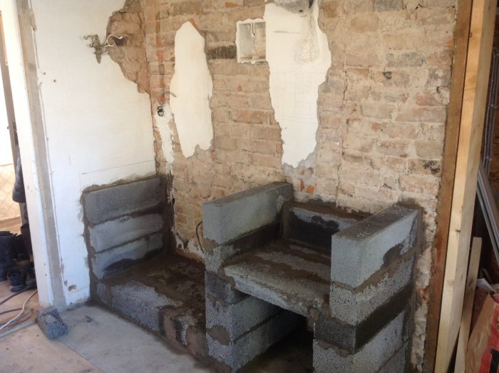Mur af Leca-blokke til pejsfundament mod en eksponeret murstensvæg med fjernet puds. Løs puds på væggen.