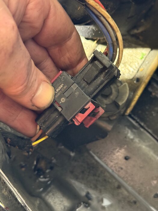 Hand håller i en kabelkontakt med flera färgade kablar, mot en bakgrund av metalliska ytor.