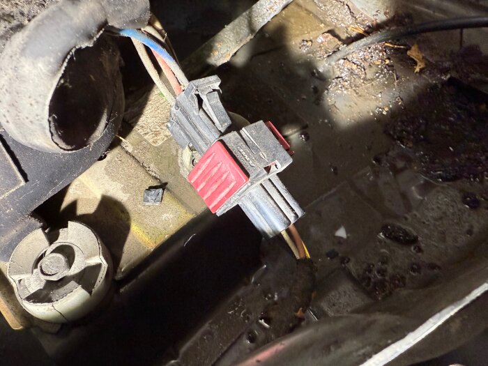 Elektrisk kontakt med röda klämmor i en smutsig, våt miljö, omgiven av kablar och mekaniska delar.
