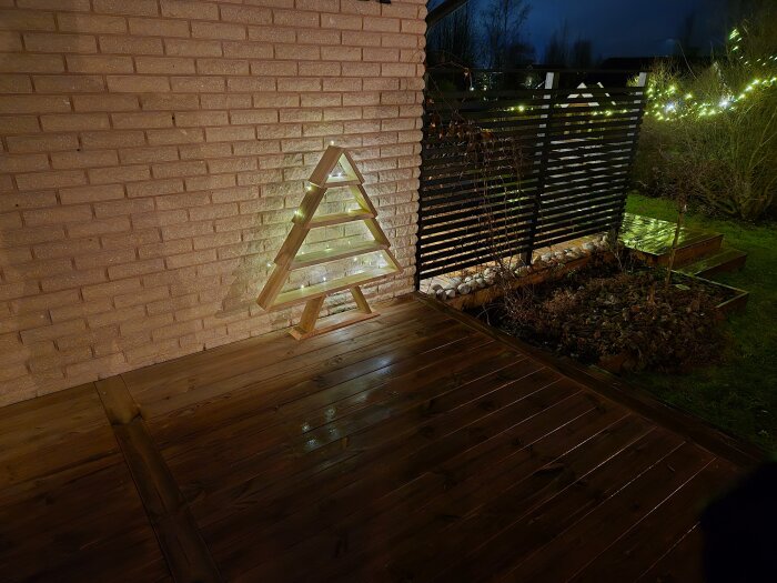 Trädformad ljusinstallation av träspill mot tegelvägg, med snökänsla från belysningen.