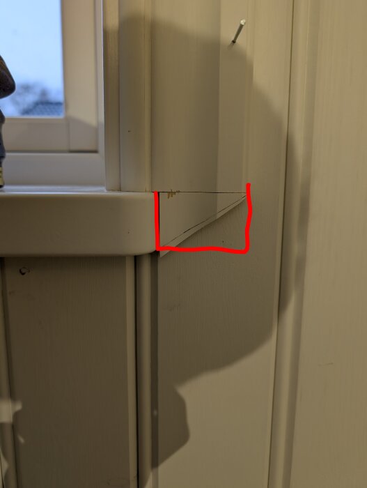 Vägg med fönsterkarm och en del av dörrpost. En röd linje markerar ett hörn mot en nyans av vitmålat trä. Penna i väggen syns också.