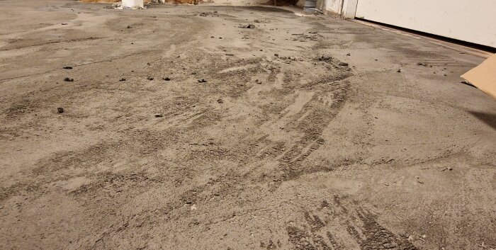 Ojämnt spacklat betonggolv i tvättstuga med synliga ojämnheter och ytor där betongen blottas. Spackel av Plane Mix S12 Rapid användes.