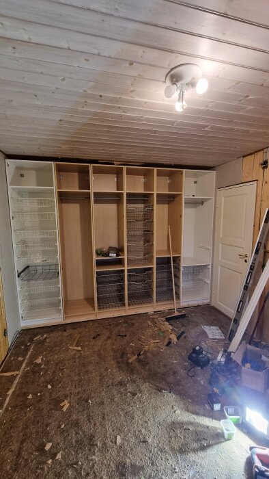 Garderober under konstruktion i ett renoverat sovrum, gips och verktyg syns på det nakna golvet, förberedelser för gipsning pågående.