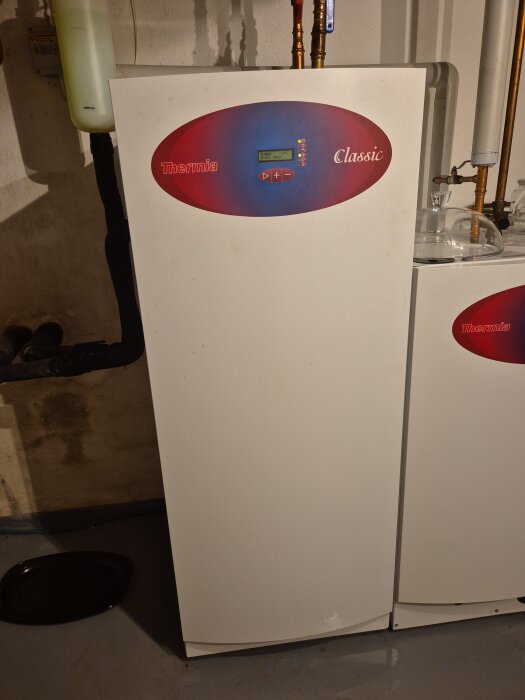 Värmepanna med röranslutningar, vattenpöl synlig på golvet bredvid.