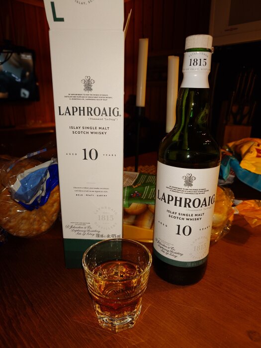 Flaska och förpackning av Laphroaig 10 år gammal whisky med ett fyllt glas framför på ett bord.