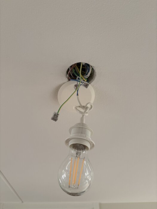 Glödlampa med synlig LED-filament hänger i sockel, ledningar syns runt takhålet, utan doslock.