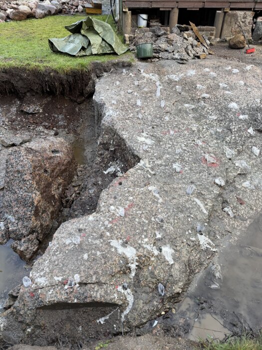Borrhål i berg för spräckning med snigeldynamit, plaststrumpor i hålen. Omgiven av jord och sten, grönt gräs till vänster.