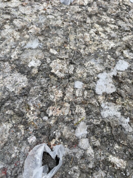 Sprucken bergyta med plaststrumpa i borrhål, använd för snigeldynamit för att bryta ner berget vid byggprojekt. Sprickor synliga på ytan.