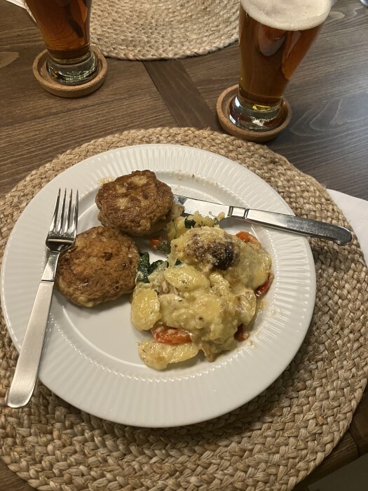 Grekiska kycklingburgare och potatisgratäng med grönsaker på en tallrik. Två glas öl på bordet.