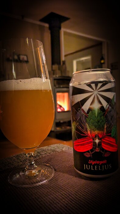 Ölglas och burk med etikett "Stigbergets Juleljus" framför en tänd vedspis i ett mysigt rum.