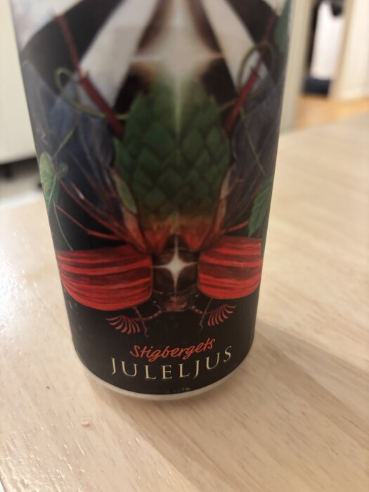 En burk med layouten "Stigbergets Juleljus," med ett insektsmotiv och text i rött på svart bakgrund, stående på ett träbord.