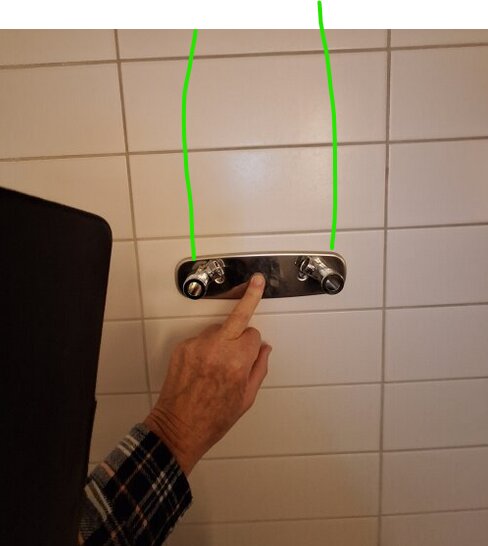 En person pekar på en platta med två vattenanslutningar på vit kaklad vägg, med gröna linjer som visar rördragning.