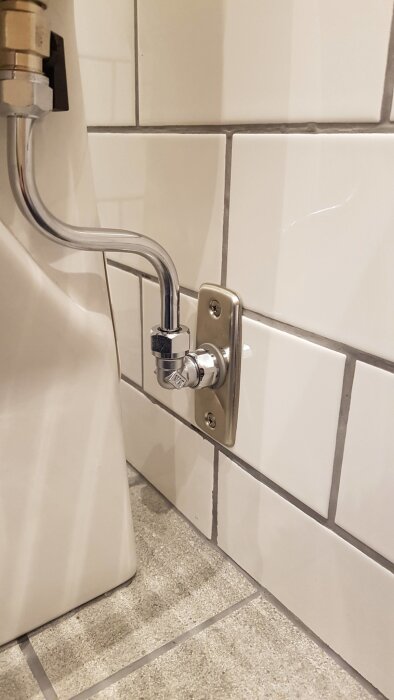 WC-ventil med lutande koppling mot kaklad vägg, kopplad med böjd metallslang. Ventilen är monterad horisontellt.