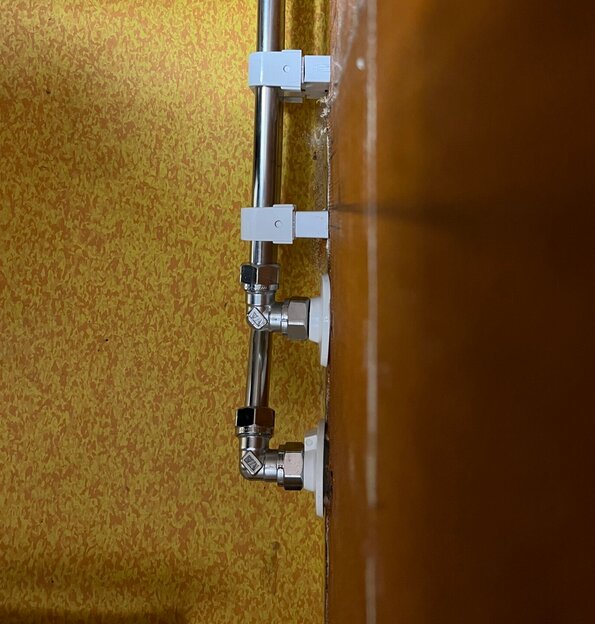 Installationsrör med fyrkantiga brickor monterade mot en gulaktig vägg.