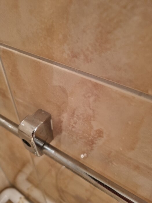 Våtrumsvägg med kakel i beige ton och duschstång i metall.