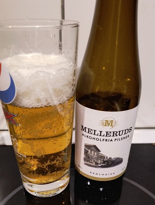 Alkoholfri pilsnerflaska från Melleruds jämte ett glas öl med skum på toppen.