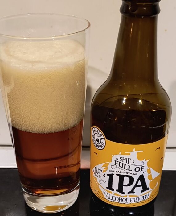 Alkoholfri IPA-flaska från Brutal Brewing och ett glas fyllt med skummande öl på en bänk.