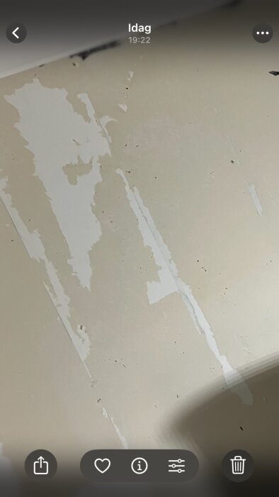 Vägg med löst bortskrapad färg, visar grundfärgen och fläckar av kvarvarande färg. Ytan är i behov av ytterligare bearbetning.