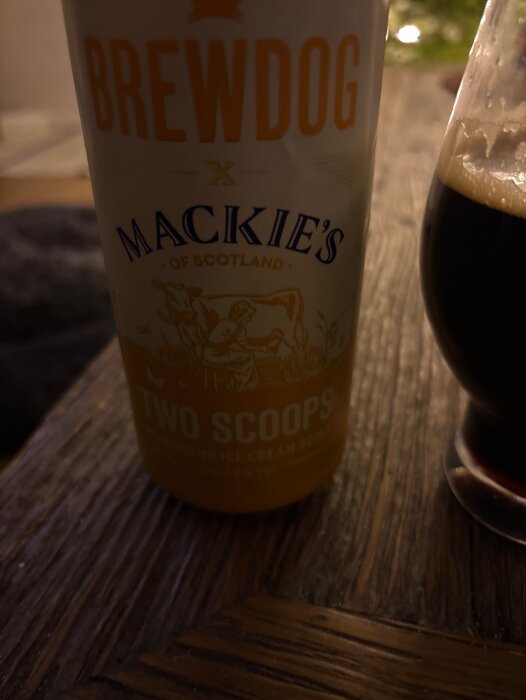 Flaska med Brewdog Mackie's Two Scoops och ett glas mörk dryck på ett träbord.