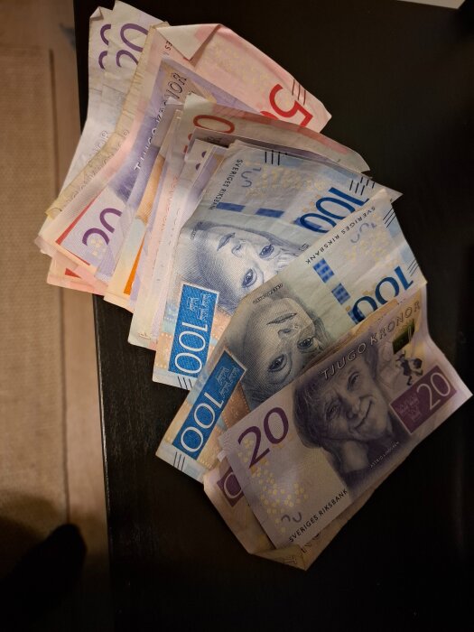En hög med svenska sedlar i olika valörer, inklusive 20-kronors- och 100-kronorssedlar, ligger utspridda på ett bord.
