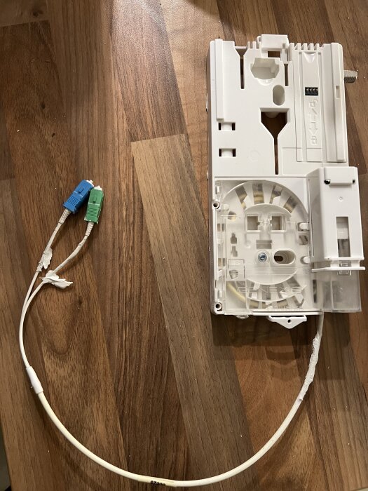 Vit fiberbox på träyta med elkablar, en grön och en blå kontakt.