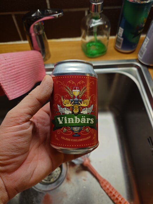 Hand som håller en röd burk märkt "Vinbärs" från Sälens Fjällbryggeri över diskbänk, med diskho och rengöringsartiklar i bakgrunden.
