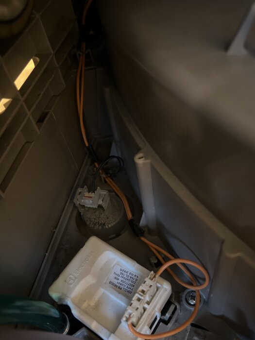 Inuti en maskin med synliga kablar, en vit komponent märkt Electrolux, och en anslutning till en grön slang.