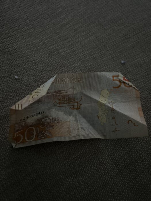 En skrynklig svensk 50-kronorssedel ligger på ett mörkt tygunderlag.