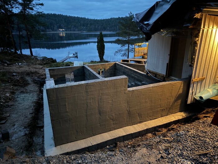 Grund för husbygge på sluttande tomt med sjöutsikt i bakgrunden. Träfasad planerad för att dölja olika nivåer.