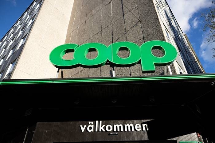 Coop-butikens fasad med dess logotyp och skylten "välkommen" under, mot en delvis molnig himmel.
