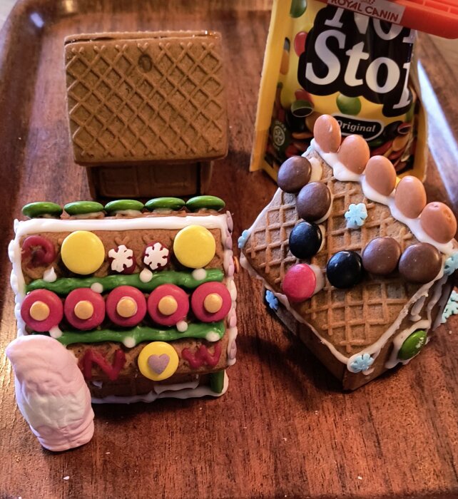 Dekorerade pepparkakshus med Non Stop-godis och glasyr på ett brickbord, ett odekorerat. Marshmallowfigur bredvid.