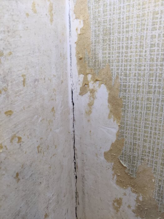 Sprukket hjørne i en vegg med delvis fjernet tapet fra et hus fra 60-tallet, viser en synlig sprikke i overflaten.