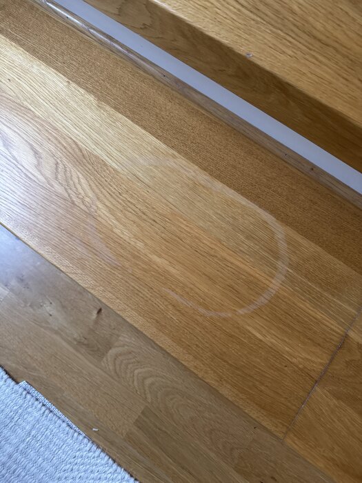 Fläck på ektrappa efter skurhink som ser blekt ut. Möjligen orsakad av vatten eller såpvatten.