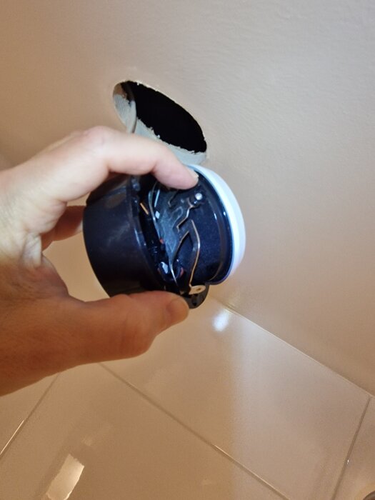 Hand lossar en infälld lampcylinder från taket, visar hål och fjädermekanism.