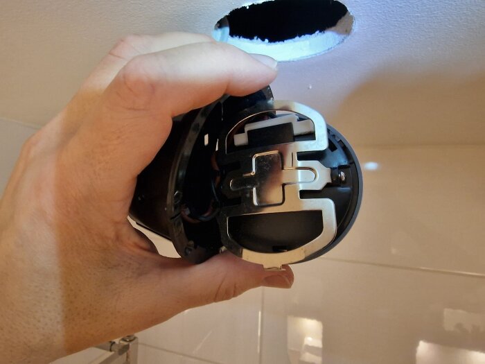 Hand som håller en taklampa med en fjäder-/bleckkonstruktion, inramad av ett hål i taket.