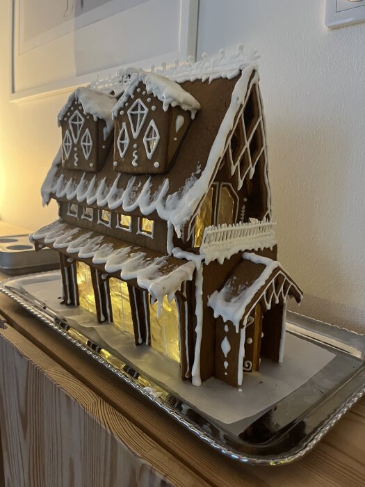 Pepparkakshus med vit glasyr och detaljerade fönster på en bricka, belyst inifrån för tävlingen.