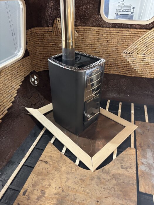 Träram under tillverkning, placerad runt en kamin med kopparplåt. Bakgrund av korkplattor och synligt ofärdigt golv.