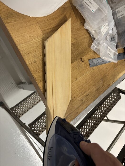Träbit med frästa spår böjs på bord med hjälp av ett strykjärn för att forma den under ett byggprojekt.