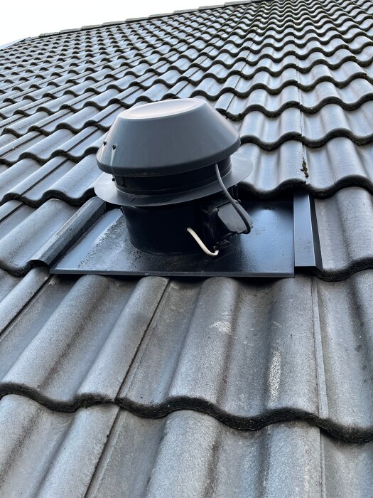 Takfläkt installerad på ett tegeltak, fotograferad i närbild. Fläkten har en rund kåpa och är monterad på en fyrkantig platta.