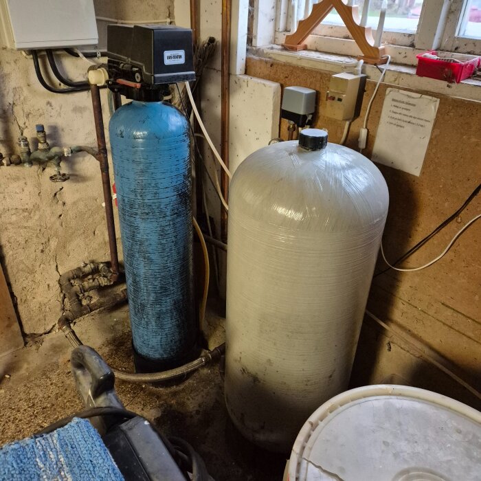 Gammalt Callidus avhärdningsfilter med blå tank och vit behållare för salttabletter i en källare.