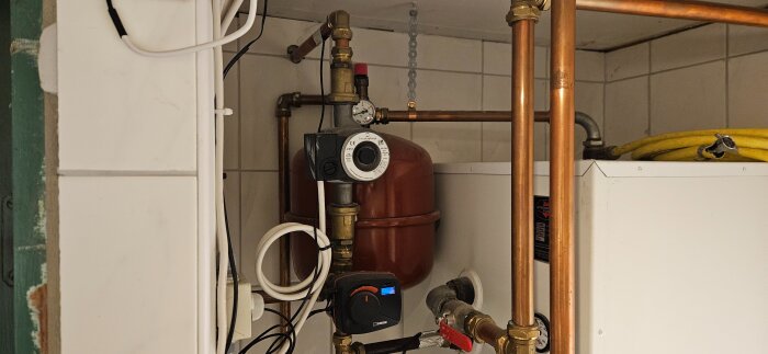 Värmepump med cirkulationspump, rörledningar och trycktank i en teknisk installation i pannrum.