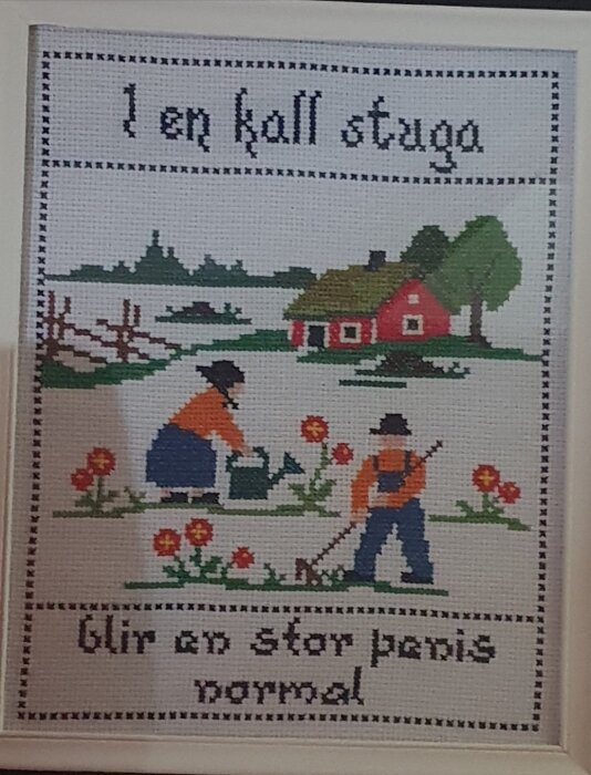 Broderad tavla med texten "I en kall stuga blir en stor penis normal" och motiv av ett par i trädgårdsarbete framför en röd stuga.