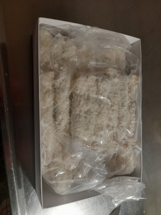 Förpackning med frysta torpedräkor inslagna i plast, placerade på en metallbänk.